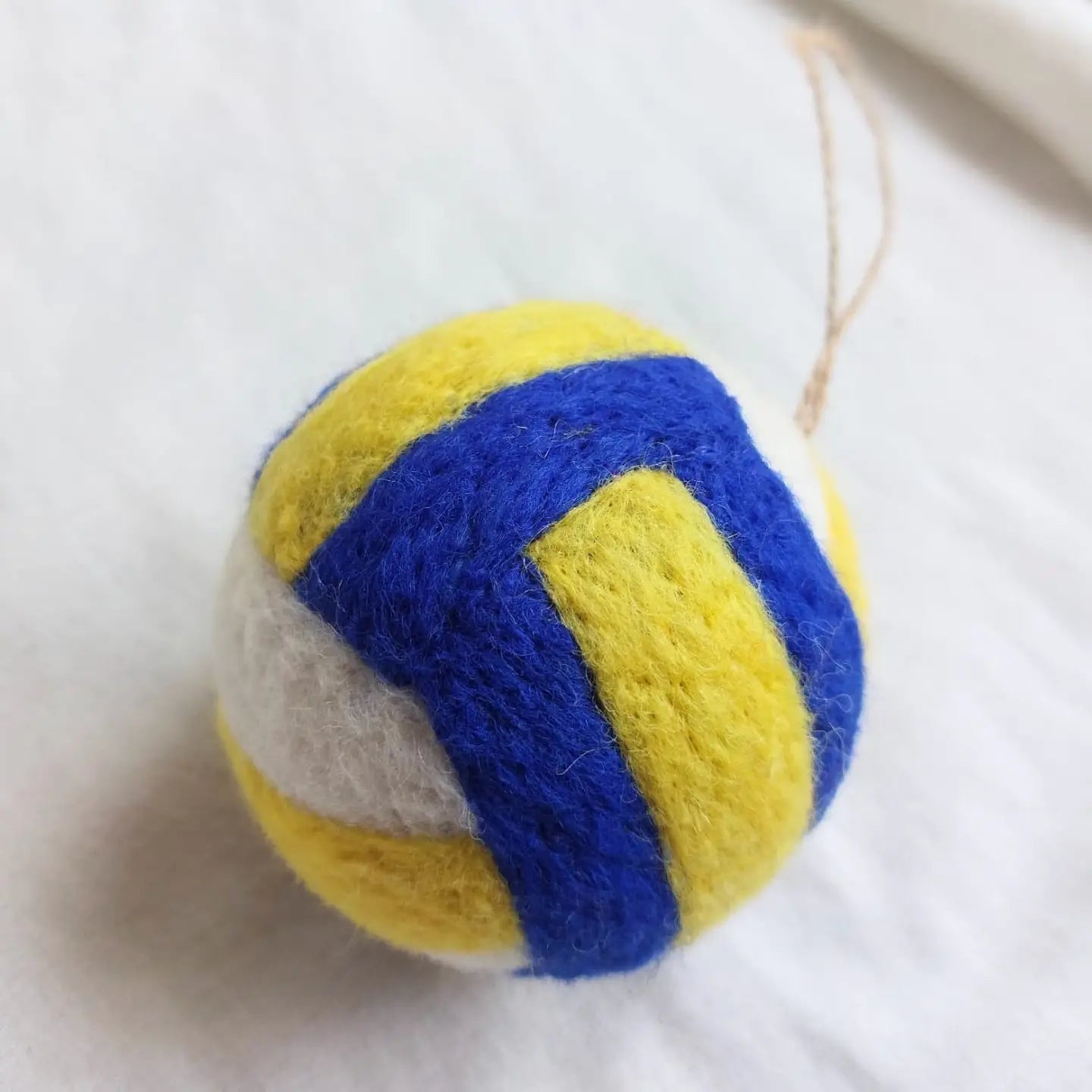 The Faire Felted Ornament features yellow, blue, and white felted sections and comes with an attached string—perfect for hanging as a Christmas ornament or adding to your collection of assorted felt ornaments.