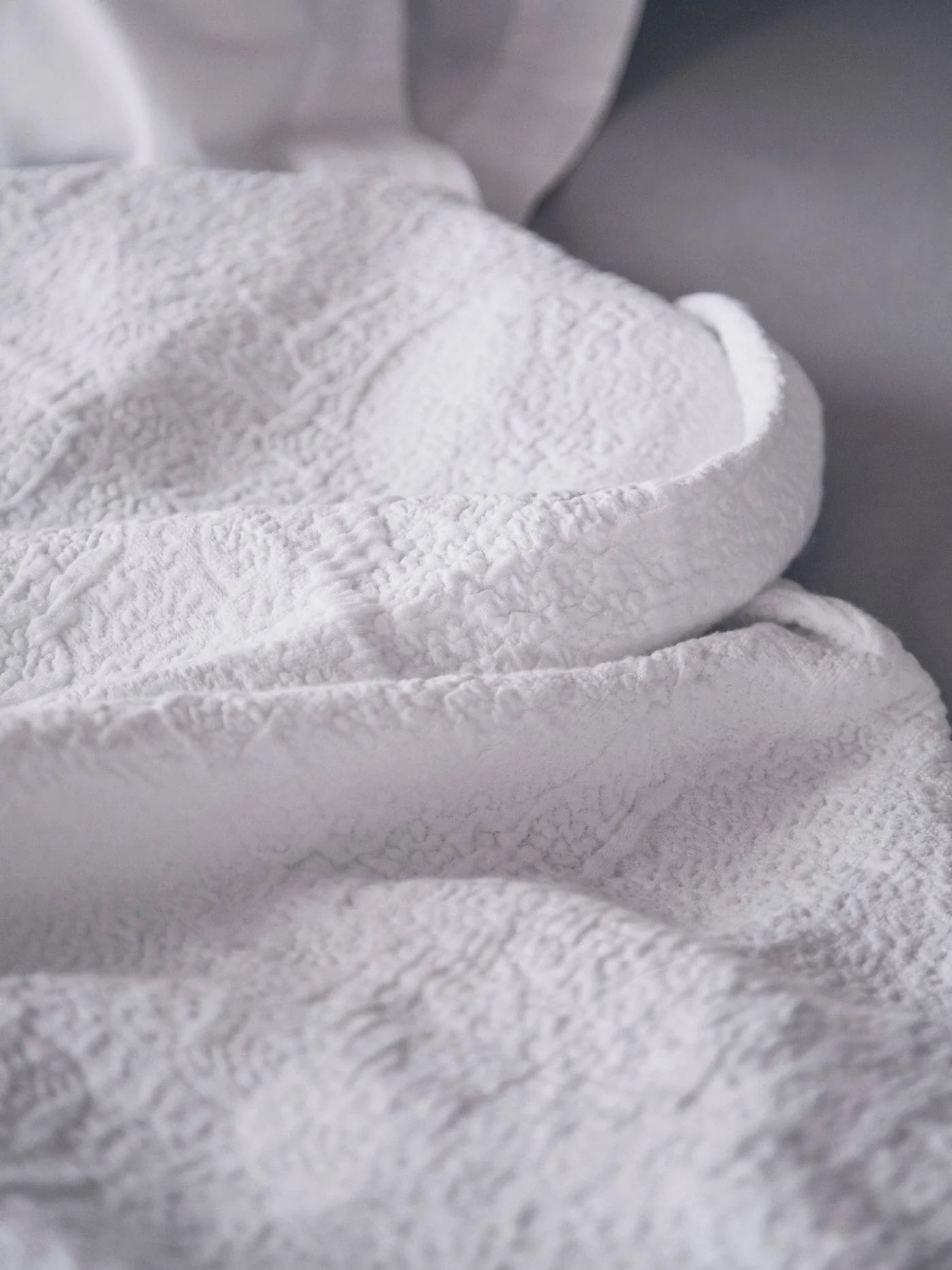 Close-up of the Antik Matelasse Coverlet by Matteo, featuring a textured white jacquard weave that forms soft folds and shadows for added depth and comfort.