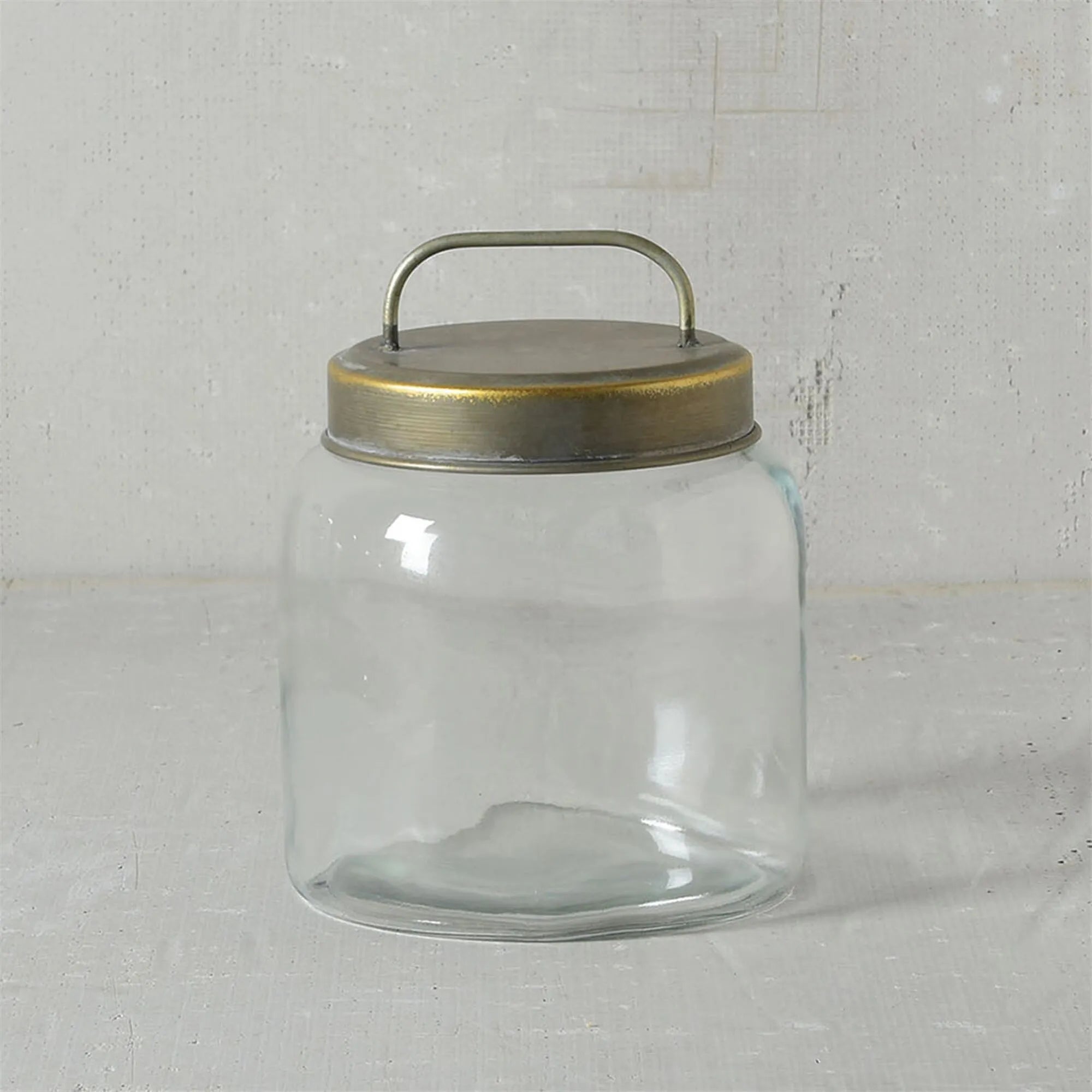 The HomArt Archer Canister Metal Lid, a clear glass jar with a wide mouth, galvanized lid, and top handle for storage, rests on a light gray textured surface against a matching background.
