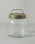 The HomArt Archer Canister Metal Lid, a clear glass jar with a wide mouth, galvanized lid, and top handle for storage, rests on a light gray textured surface against a matching background.