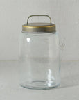 The Archer Canister Metal Lid by HomArt is a clear glass jar with a galvanized lid and small handle, shown on a light surface against a textured gray background. This empty cylindrical jar blends simplicity and functional style for perfect storage.