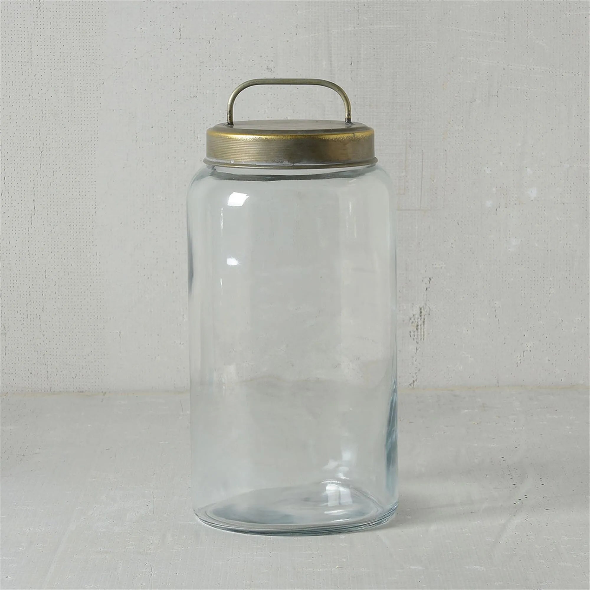 The HomArt Archer Canister with a round, galvanized metal lid and curved handle is a stylish clear glass jar, ideal for chic storage, set against a light textured background.