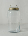 The HomArt Archer Canister with a round, galvanized metal lid and curved handle is a stylish clear glass jar, ideal for chic storage, set against a light textured background.