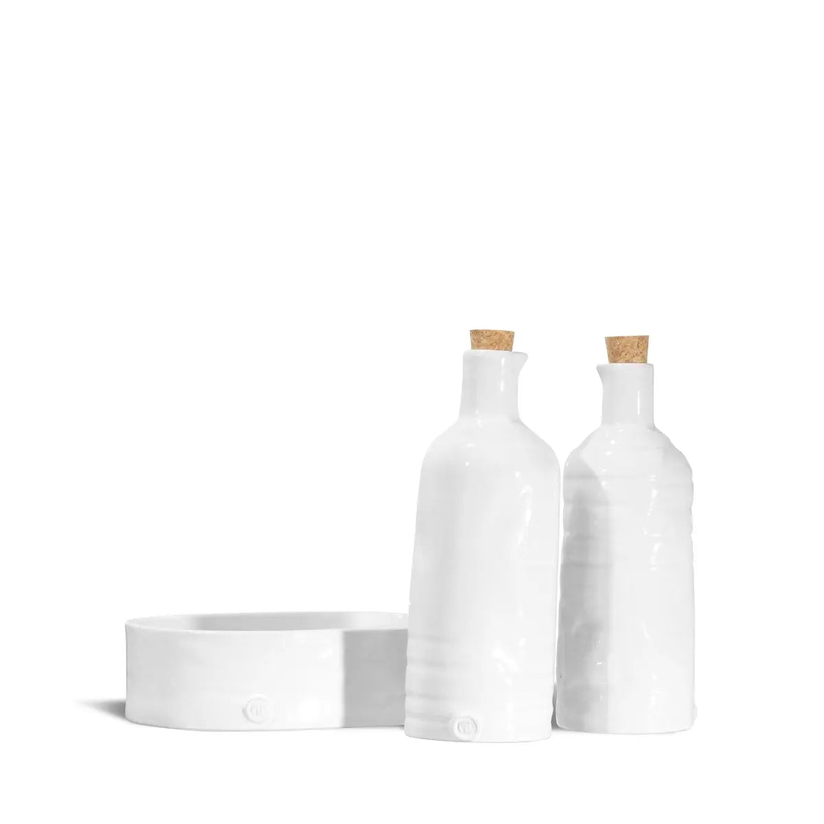 The Montes Doggett Oil & Vinegar No. 6 set includes two tall white high-fired ceramic bottles with cork stoppers and a shallow round dish, all displayed on a white background. Dishwasher safe for easy cleaning.