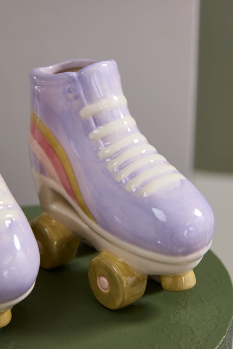 The Accent Decor Rollerskate Planter features a pastel purple ceramic skate with yellow wheels and a rainbow stripe, shown on a green surface—an ideal gift for plant lovers or as a fun Ceramic Planter.