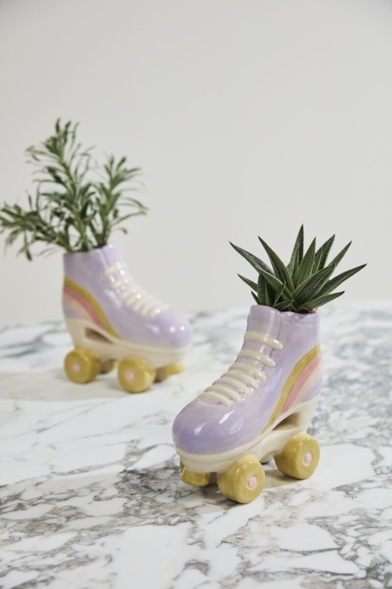 The Accent Decor Rollerskate Planter set features two pastel ceramic skates with yellow wheels, each with a small plant, displayed on a white marble surface—an adorable and perfect gift for plant lovers.