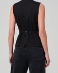 A person is seen from the back wearing a black Jasmin Long Vest by Citizens Of Humanity/AGOLDE, styled with tonal dressing. The vest features a slit and is complemented by black jeans with visible back pockets. This ensemble stands out against a plain gray background, highlighting its sleek simplicity and elegance.