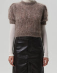 Someone wears the odette puff sleeve sweater by Citizens Of Humanity/AGOLDE, layered over a long-sleeved cream turtleneck and paired with a high-waisted black leather skirt, set against a plain light background.
