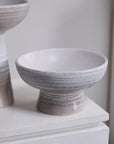 The Lorca Footed Bowl by Accent Decor features a sturdy base and wide, shallow shape with a white-to-light gray gradient, making it ideal for home decor or stylish bowl fillers. It sits elegantly on a white surface beside a similar vessel.