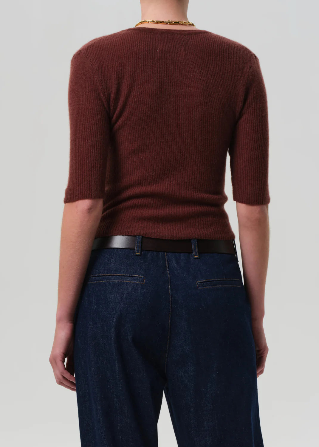 A person is seen from the back wearing the Tabitha Cardigan by Citizens Of Humanity/AGOLDE and dark blue jeans with a black belt, standing against a plain light gray background.