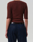 A person is seen from the back wearing the Tabitha Cardigan by Citizens Of Humanity/AGOLDE and dark blue jeans with a black belt, standing against a plain light gray background.