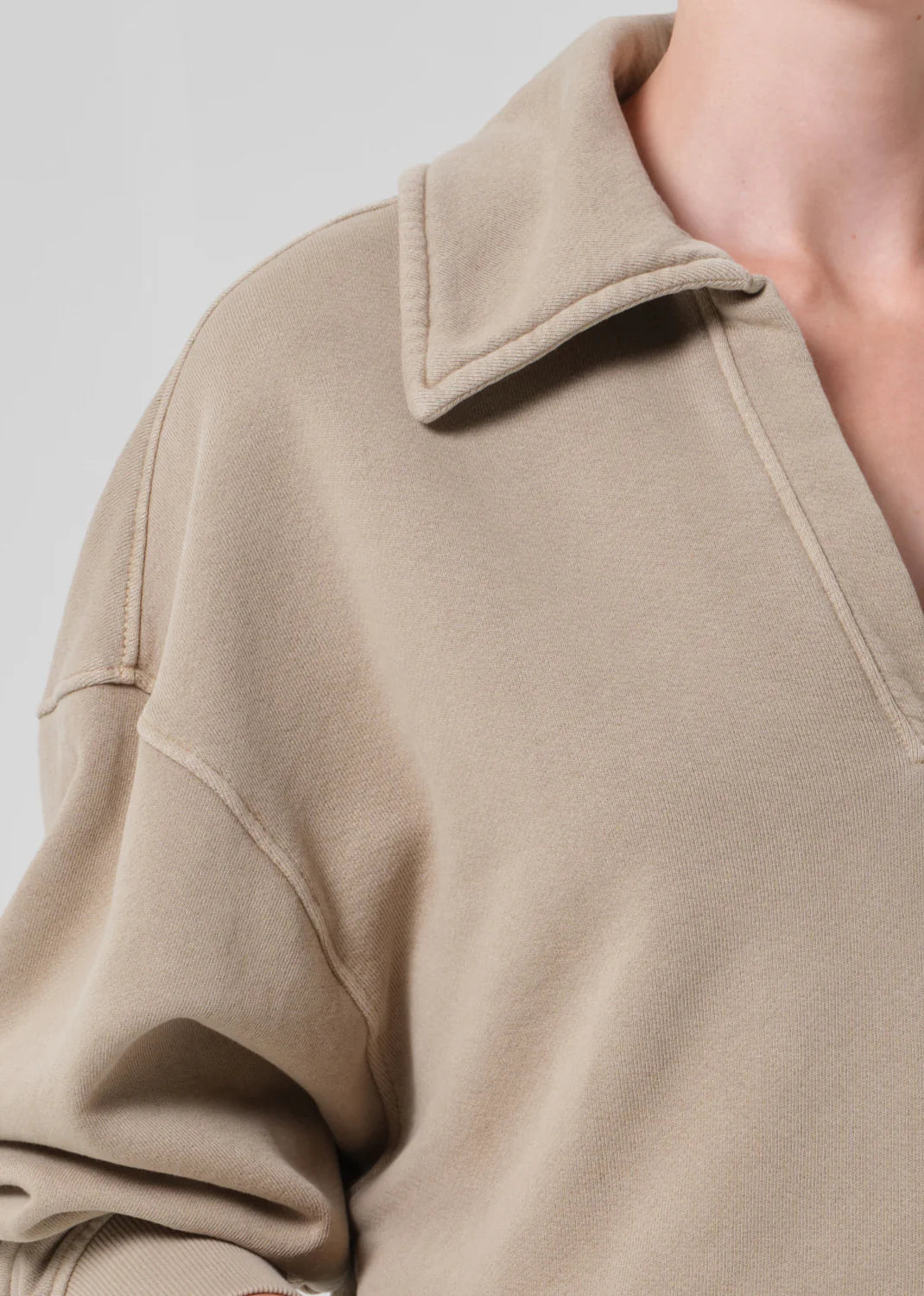 A close-up of a person wearing the Citizens Of Humanity/AGOLDE trapeze pullover—a beige, collared, long-sleeve sueded fleece with a relaxed fit. The image highlights the upper chest, shoulder area, open collar, and soft texture.