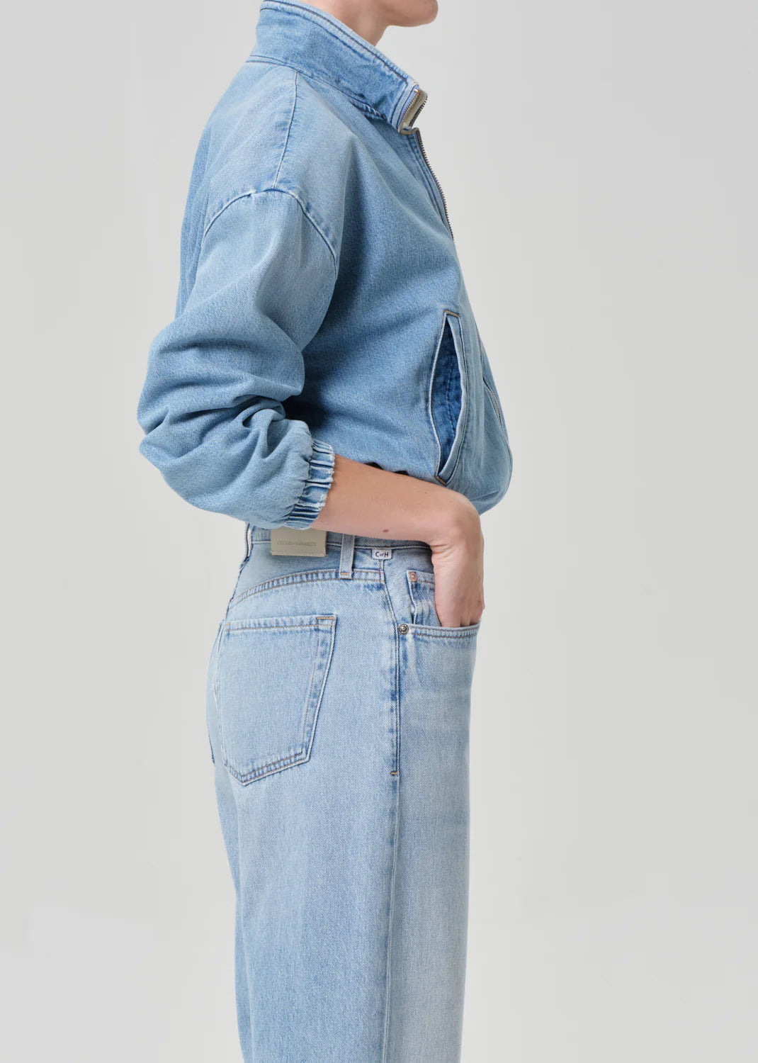 Wearing the bubble bomber in marseille by Citizens Of Humanity/AGOLDE and matching high-waisted jeans, a person stands in profile against a plain background, hand in pocket and face partially out of frame.