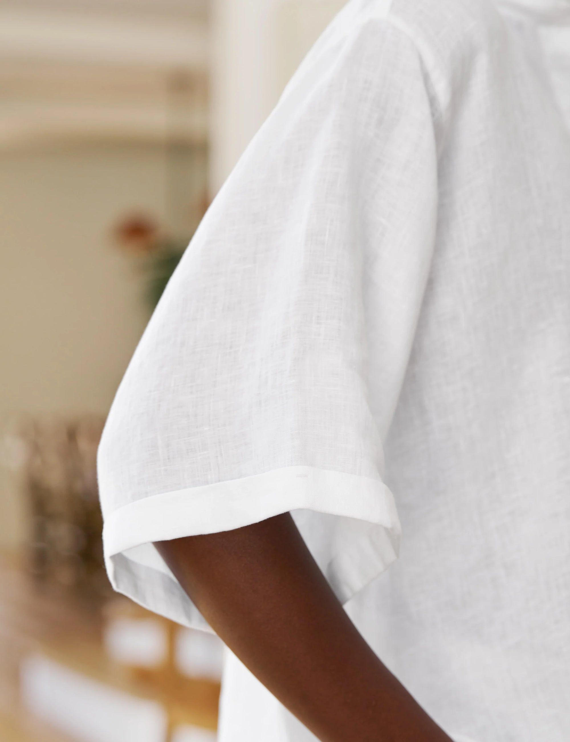 Close-up of a person wearing the Frank & Eileen ROSIE SS Button Up F25—a versatile, loose-fitting white linen short sleeve shirt. The focus is on the arm and sleeve against a softly blurred background.