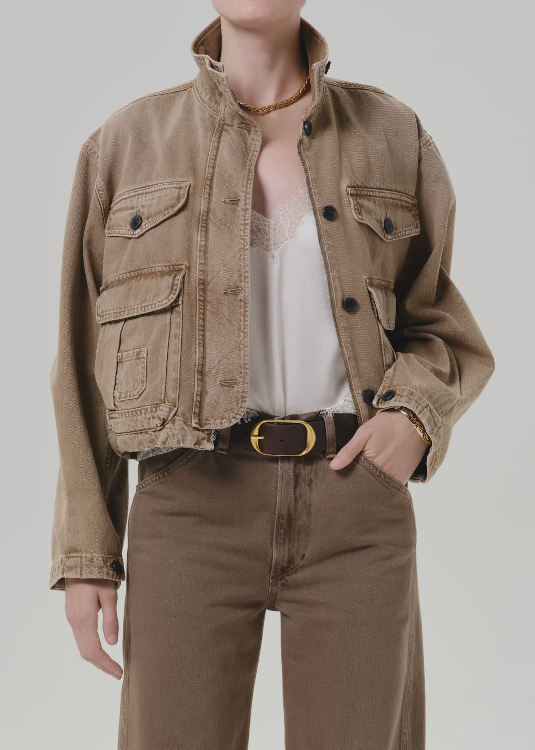 Tan Citizens of Humanity barn jacket with white lace top, brown pants, and gold-buckle belt in a modern setting.