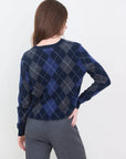 A person with long brown hair, seen from behind, wears the Brazeau Tricot Argyle V-Neck sweater in navy and gray with gray pants against a plain white background.