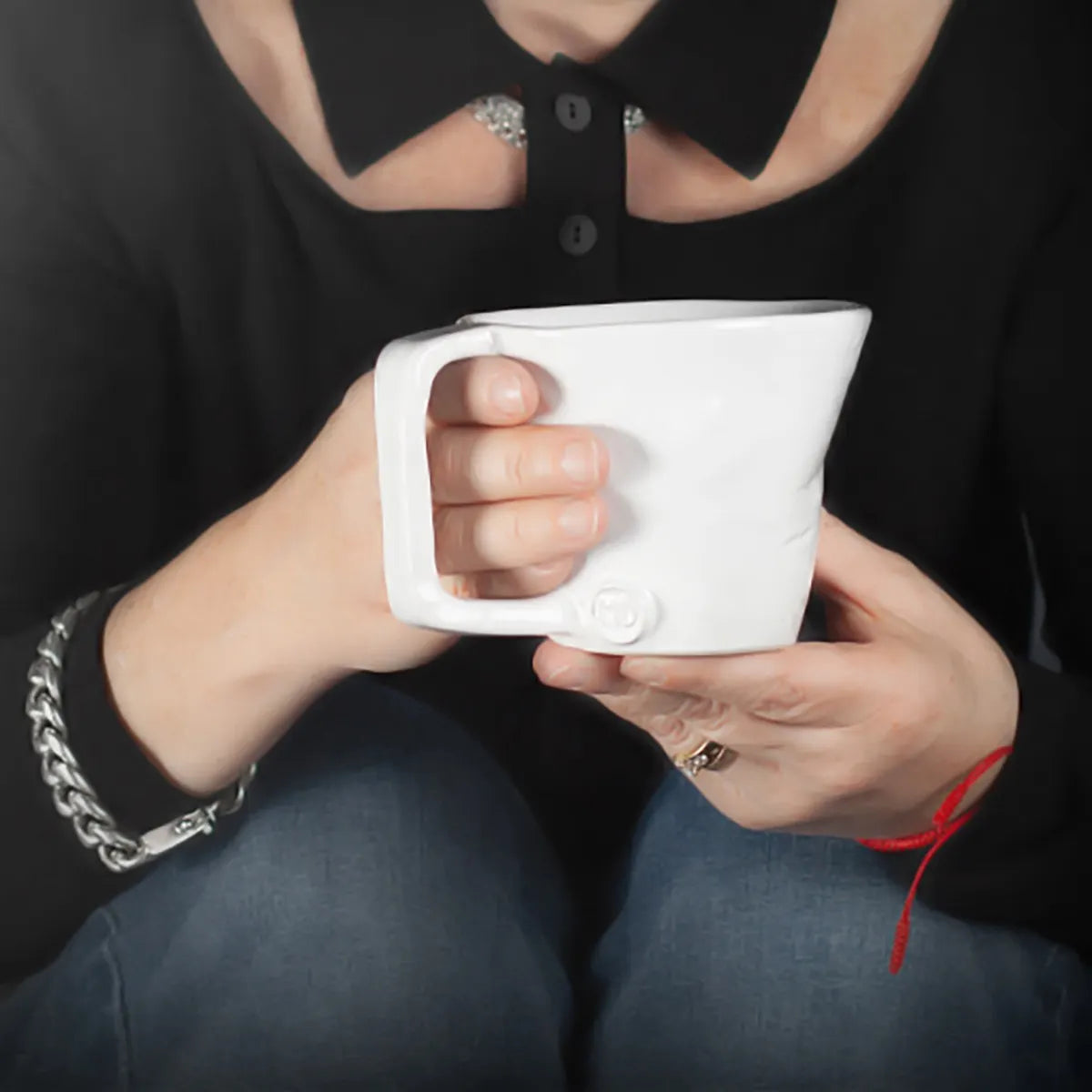 A person holding the Montes Doggett Mug No. "379"—a large, white, microwave-safe mug—with both hands is seen wearing a black top, blue jeans, silver bracelet, ring, and red string bracelet. Their face is not visible.