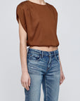 A person wearing the Moussy MV Satin Shell Cap Top—a loose brown, versatile short-sleeve piece—with blue jeans stands against a plain light gray background. The face is not visible.