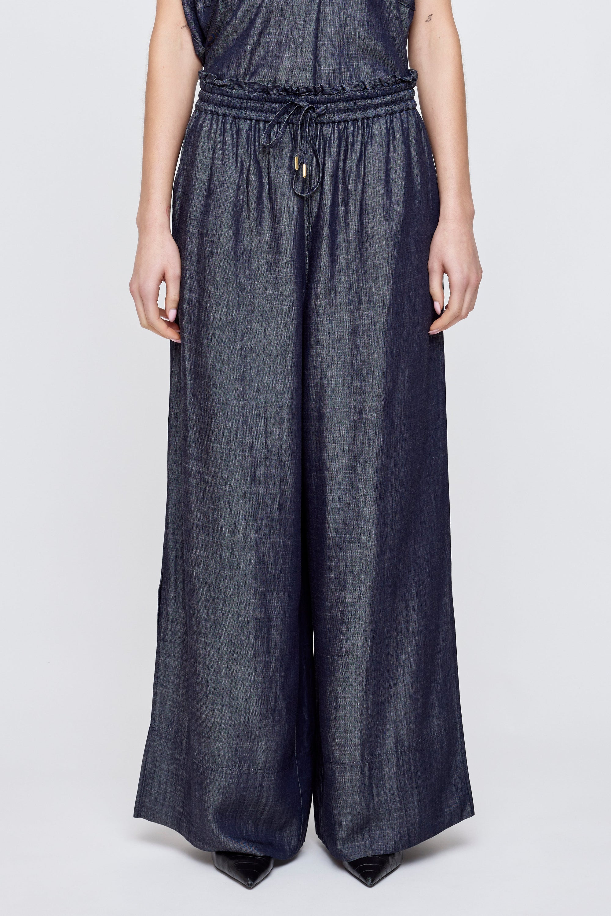 A person models Moussy High Waist Denim—wide leg jeans with an adjustable drawstring waist—against a plain light background, showing only the lower torso and legs.