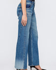 A person stands sideways against a white background wearing Moussy's Holyoke Panel Wide high-waisted, wide-leg blue jeans with raw hems and black pointed-toe heels.