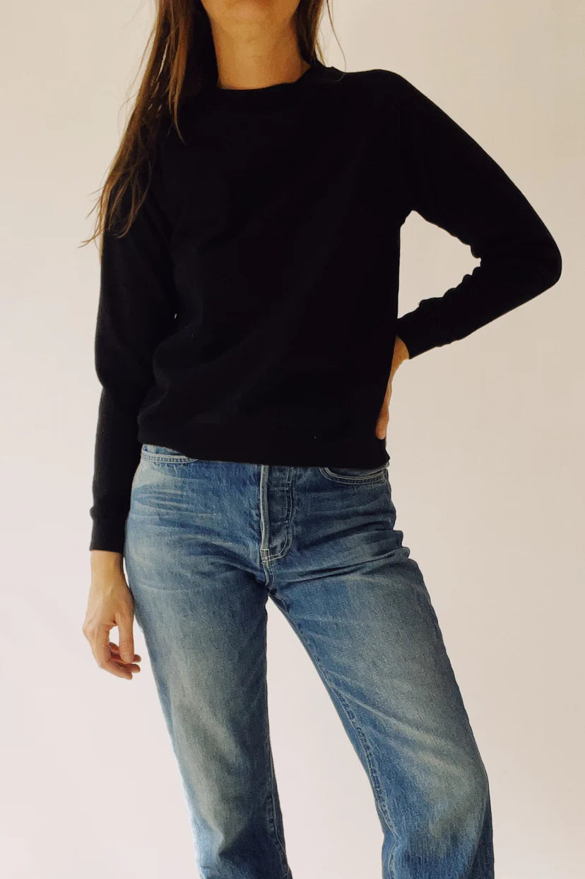 A person wearing *The Sweatshirt* by Hey Gang and blue jeans stands against a plain background with one hand on their hip.