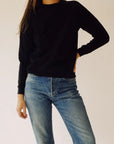 A person wearing *The Sweatshirt* by Hey Gang and blue jeans stands against a plain background with one hand on their hip.