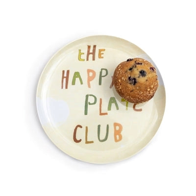 The Breakfast Club Plate Set by Sugarboo Designs features a beige plate with colorful "The Happy Plate Club" text and a blueberry muffin on the upper right, perfect for a champion-worthy breakfast.