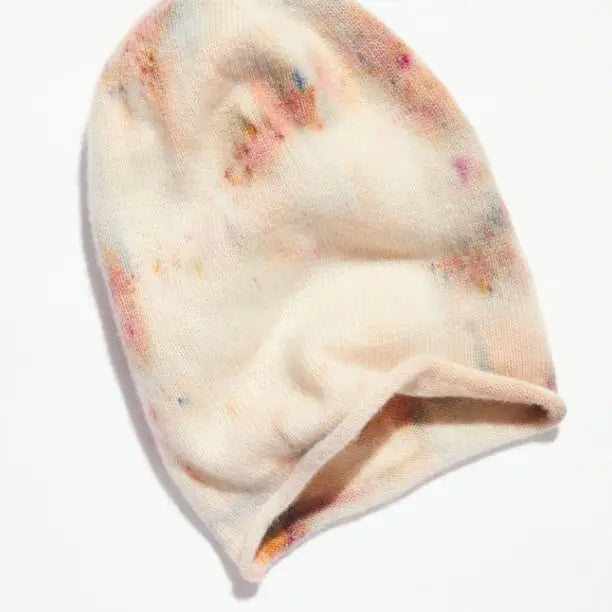 The Faire Cashmere Beanie is a soft, hand-dyed cream hat with subtle pastel tie-dye patterns, shown flat on a white background. Made in the USA.