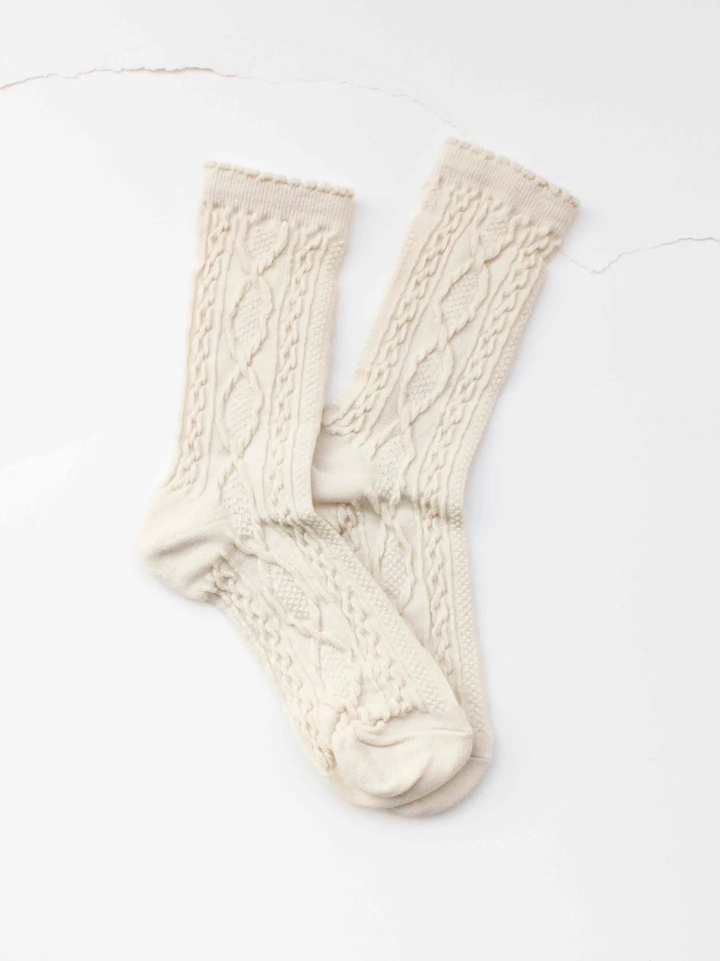 Faire Twist Cotton Crew Socks in cream feature a textured cable knit pattern and are shown overlapping on a white surface.