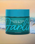 A teal jar of Faire's Tallow Face Balm Moisturizer sits before ocean waves. Made with grass-fed tallow for daily glow, "Darlin" is written in bold script across the jar.