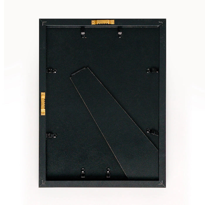 A black Faire frame, shown from the back with metal clips, a stand, and hanging hardware, is ready to display Cezanne’s "The Peppermint Bottle"—ideal for showcasing limited-edition art against a plain white background.