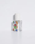 The Maison Matine Perfume by Faire features a clear bottle with a white speckled cap and vibrant abstract designs, displayed on a white surface against a plain background, suggesting bergamot notes in its delicate scent.