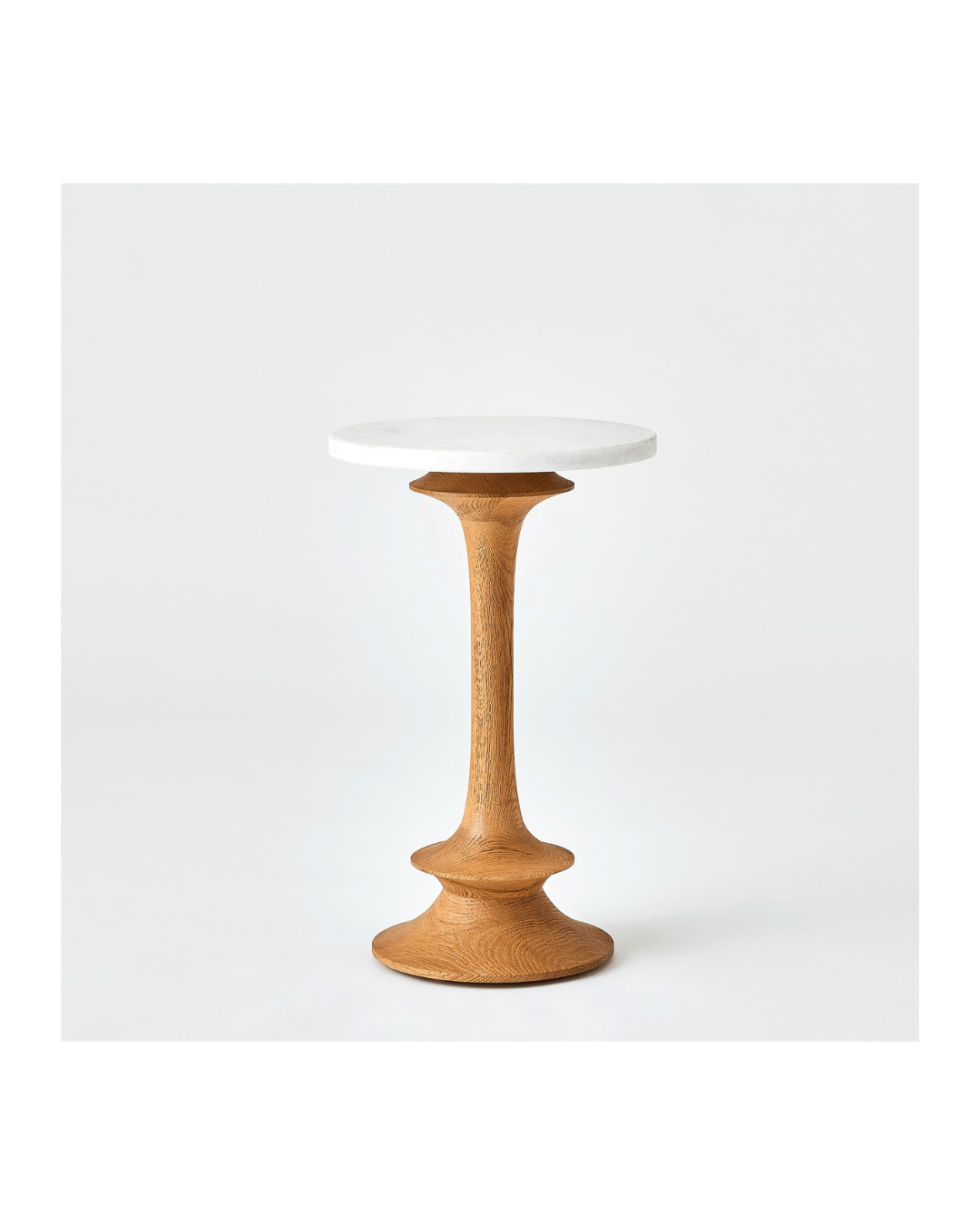 The Oasis Side Table-Natural-Small by Global Views features a small round white marble top and a sculpted solid oak wooden pedestal base. Its minimalist design and natural finish offer modern elegance, highlighted against a plain white background.