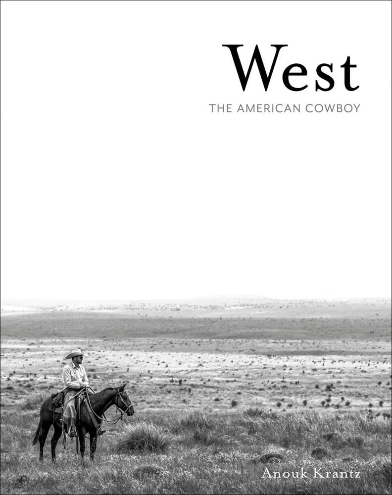 A black-and-white image of a cowboy on horseback in an expansive landscape embodies fine art photography, capturing the Wild West's spirit on the cover of Anouk Krantz's "West: The American Cowboy," published by National Book Network.