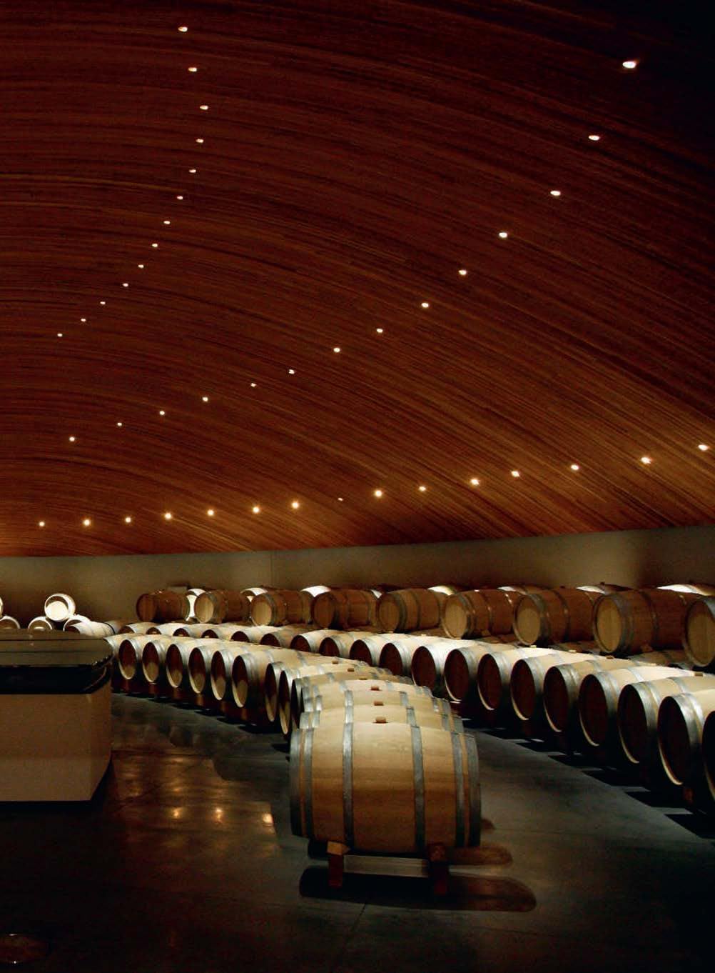 A dimly lit wine cellar with arched wooden ceilings and rows of barrels sets the perfect scene for wine lovers, much like the destinations in "150 Vineyards You Need" by Simon & Schuster Inc.