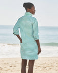 A woman stands on a sandy Southern Ireland beach, facing the ocean in the Frank & Eileen Southern Dress. Her hair is tied back as gentle waves roll in behind her.