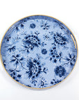 The Blue Floral Round Tray by Faire showcases a vibrant blue floral pattern set against a light blue background, accentuated by an elegant shiny gold rim. The intricately designed flowers provide classic beauty and sophisticated organization, making it perfect for any decor setting.