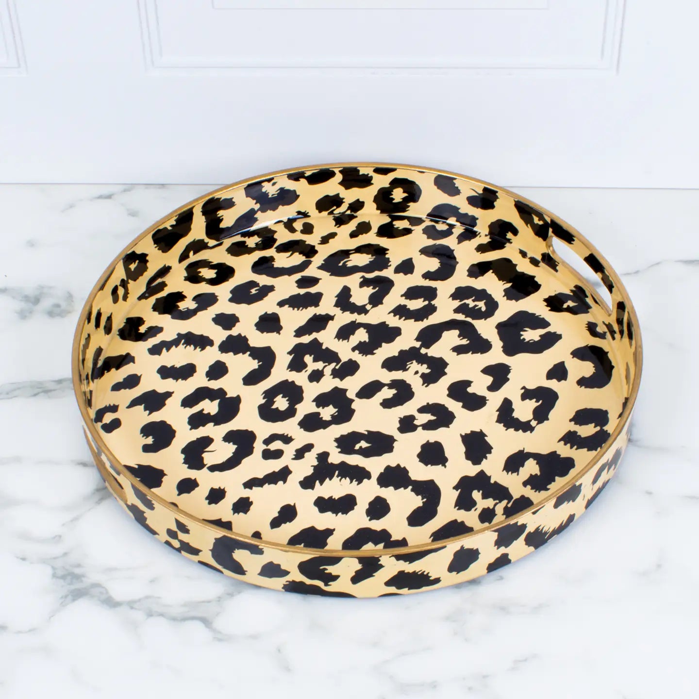 The Leopard Round Tray by Faire is a chic decorative tray featuring an animal print design with black spots on a beige background. It rests elegantly on a marble surface and has a glossy finish, making it ideal for adding a stylish touch to any space.