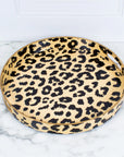 The Leopard Round Tray by Faire is a chic decorative tray featuring an animal print design with black spots on a beige background. It rests elegantly on a marble surface and has a glossy finish, making it ideal for adding a stylish touch to any space.