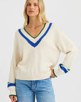 A woman with long blonde hair models the One Grey Day Venus V Neck, a vintage-inspired cotton sweater with blue and green stripes, paired with light blue jeans against a plain white background.