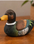 Brown hand-painted carved basswood duck by The Faire brings rustic charm to a table, plant softly blurred behind.
