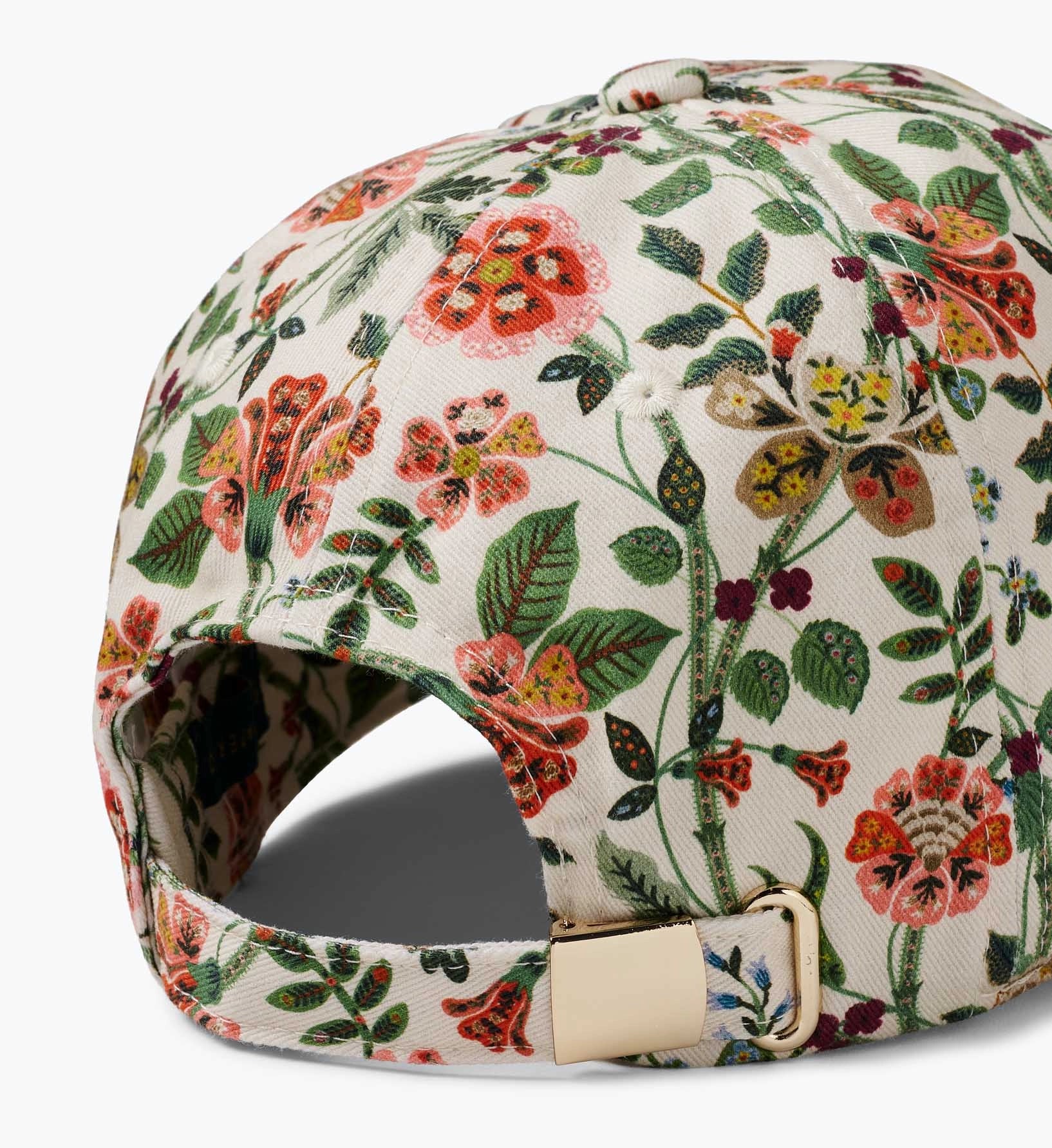 A close-up of the Gracie Baseball Cap by Faire highlights its cream color, vibrant floral print, and an adjustable strap featuring a gold metal buckle.