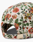 A close-up of the Gracie Baseball Cap by Faire highlights its cream color, vibrant floral print, and an adjustable strap featuring a gold metal buckle.