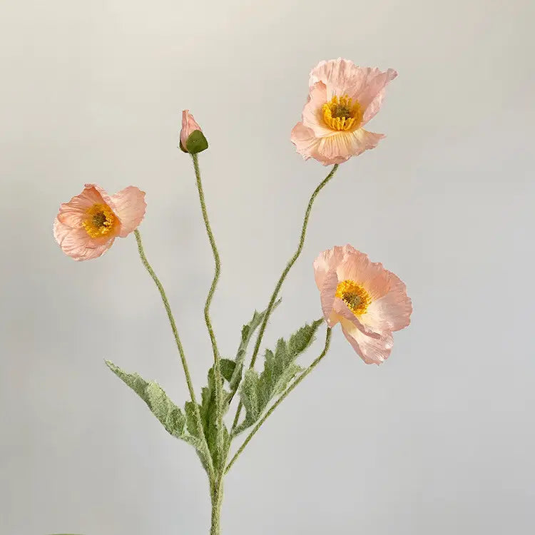 The 22'' Single Flocked Floral Poppy Spray by Faire features delicate pink silk flowers with yellow centers and green stems, including an artificial poppy and unopened bud, arranged against a light gray background.
