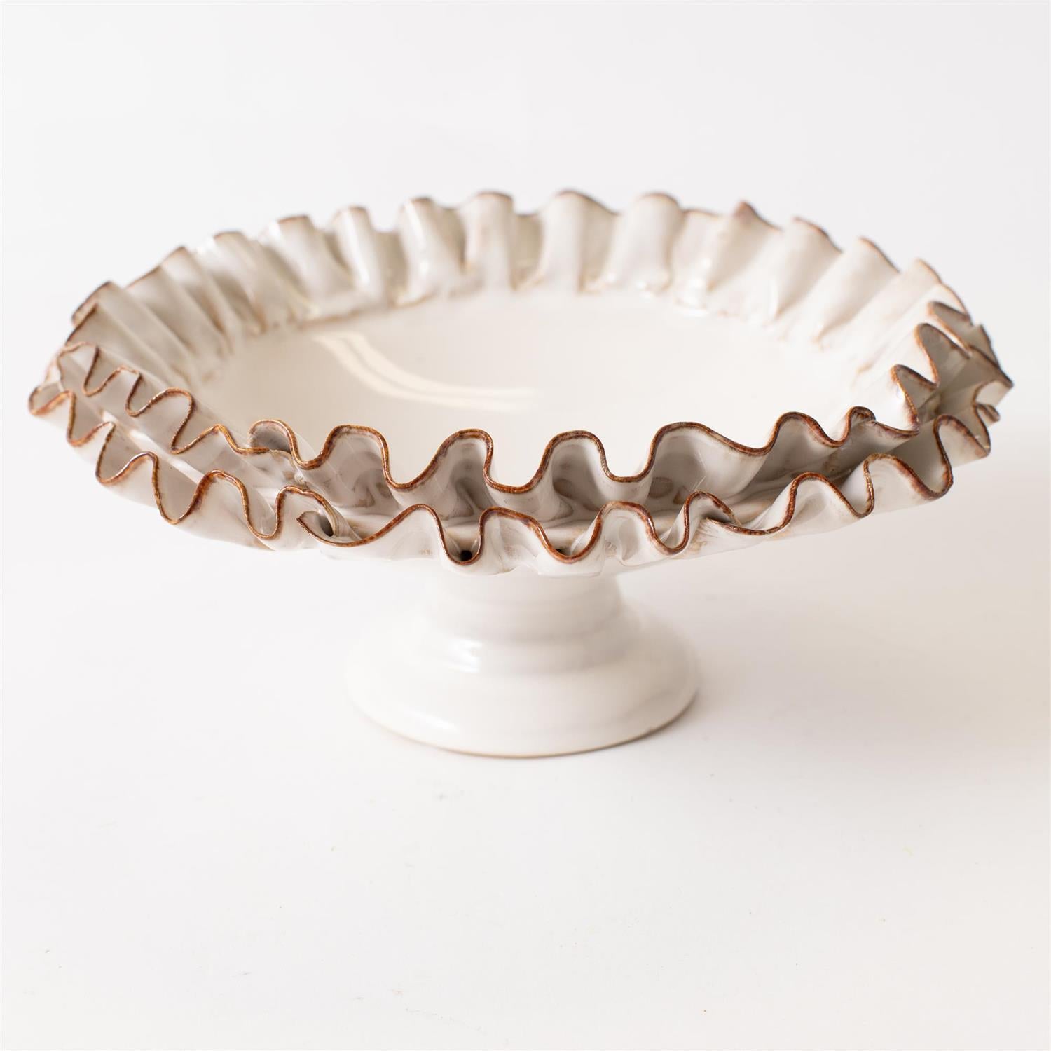The Compote with Ruffles by Faire features a white ceramic design with a ruffled edge, short pedestal base, and brown-accented rim for rustic charm. Handcrafted home decor shown on a plain white background.