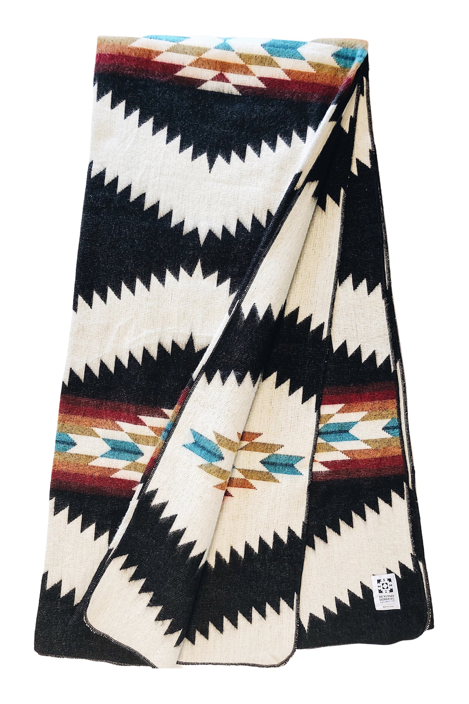 The Tsachila Blanket by Faire is a folded recycled acrylic throw with bold black, white, brown, blue, and red zigzag and diamond patterns—ideal for boho decor. A fabric tag is visible on one corner.