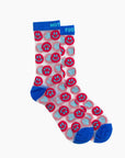 The Step Up Sock by Mother features white tube socks with blue cuffs, heels, and toes, a repeated red smiley face pattern with blue and white accents, black stars on a translucent grey band.