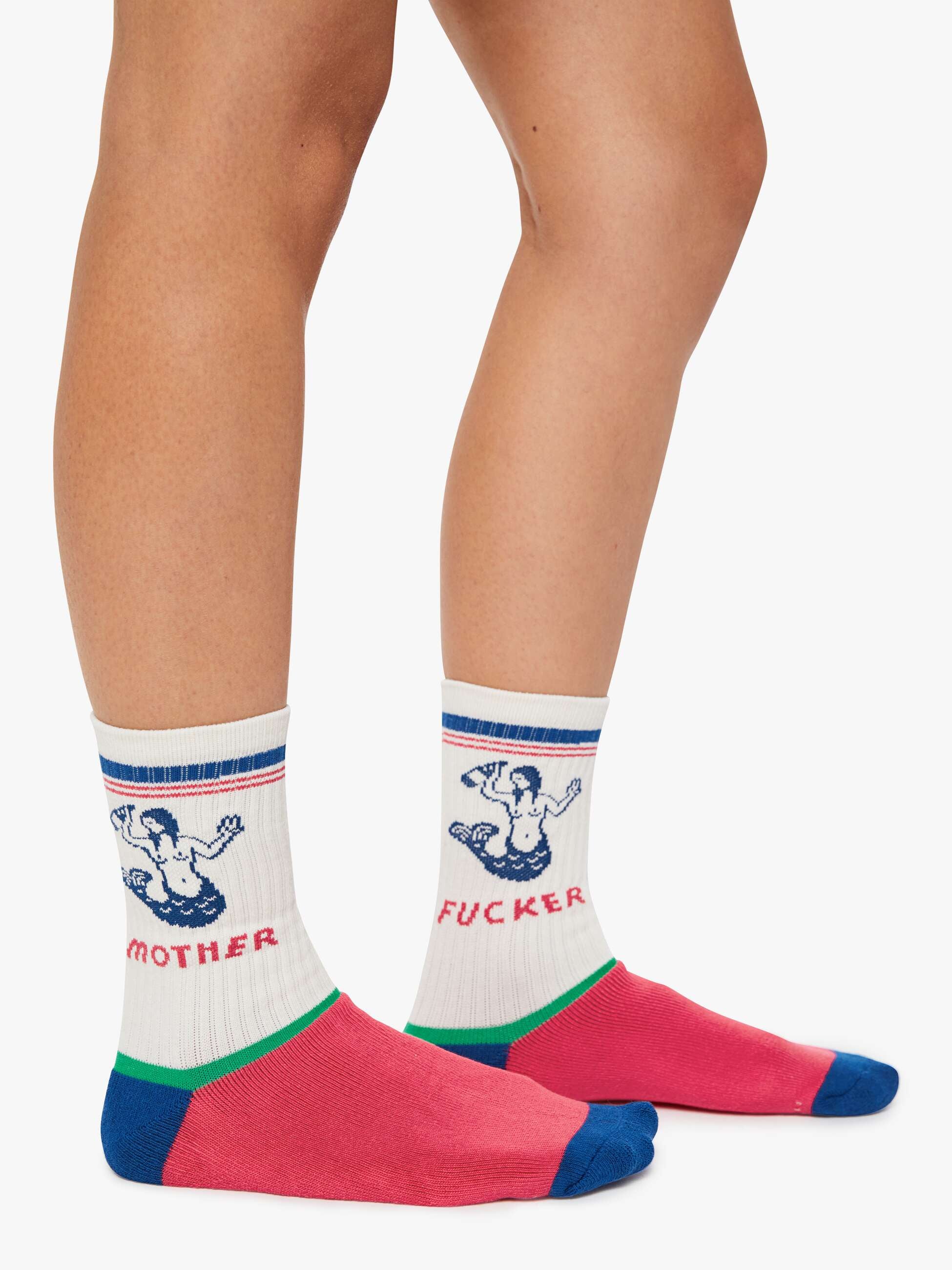 Two legs wear The Half-Calf Swim Club socks by Mother—white tube socks with blue and red stripes, pink toes, blue heels, and bold blue graphics of hands spelling “MOTHER” on one and “FUCKER” on the other.
