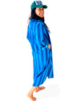 A person stands barefoot, smiling over their shoulder, wearing a green "SUN" cap and the Faire Surf Stripe Shirt Dress.