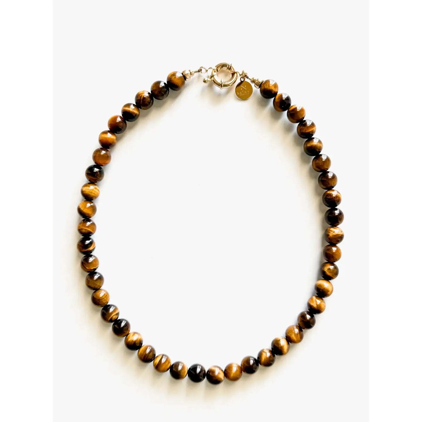 The Galleria Necklace by Faire features polished round tiger's eye beads with brown and gold bands, finished with gold plated findings and a small round tag, shown on a plain white background.
